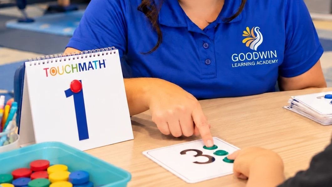 A Goodwin Learning Academy teacher pointing to the dots on a TouchMath number card as a student touches them